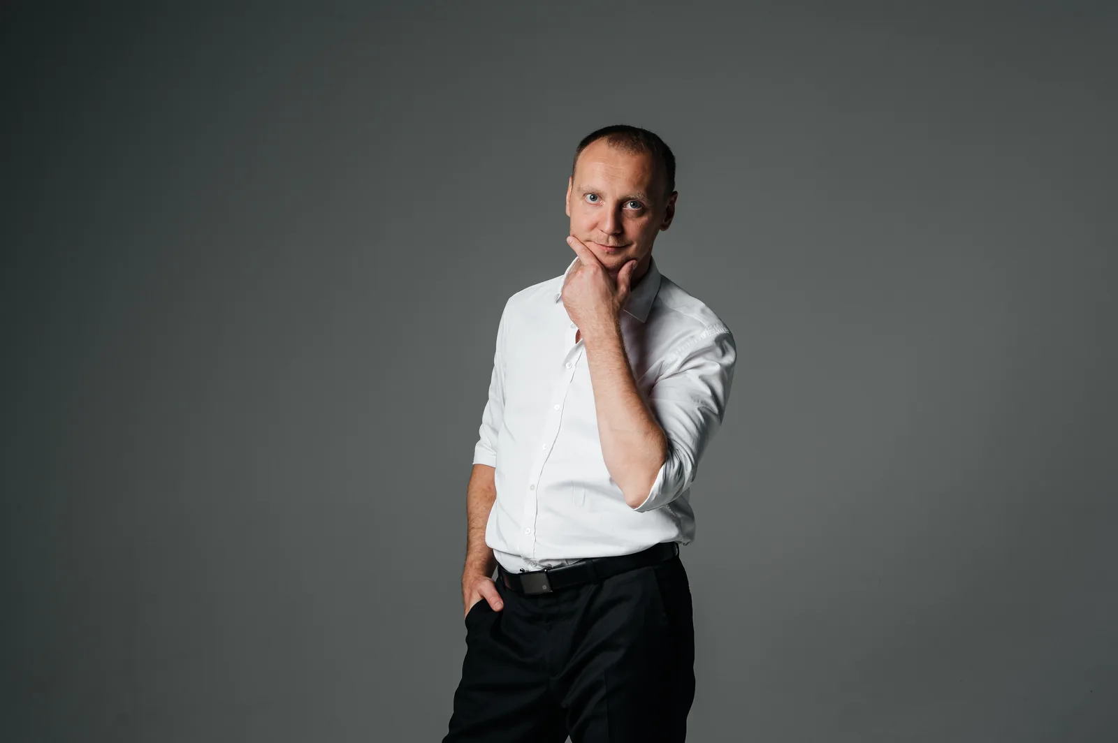 Адвокат в белой рубашке с рукой у подбородка, портрет для страницы о представительстве в арбитражном процессе